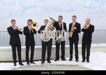 Brass band de six musiciens en costumes jouent de la musique sur le toit d'un grand bâtiment le jour d'hiver Banque D'Images