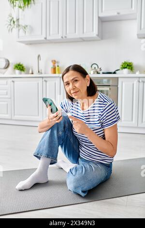 Une femme en tenue confortable est assise sur le sol, engrossée dans son téléphone portable. Banque D'Images