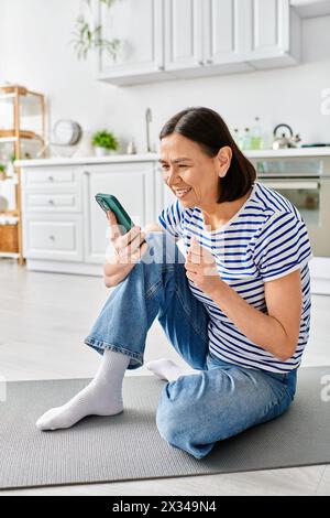 Une femme mature dans des vêtements confortables se trouve sur le sol, engrossée dans son téléphone portable. Banque D'Images