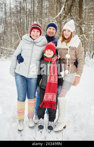 Famille heureuse de quatre stands embrassant sur des patins sur la voie de glace dans le parc d'hiver. Banque D'Images