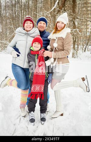 Famille heureuse de quatre stands embrassant sur des patins sur la voie de glace dans le parc d'hiver. Banque D'Images