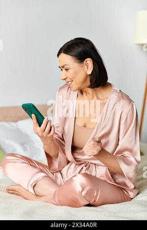 Femme dans des vêtements confortables assis sur le lit, engrossée dans le téléphone portable. Banque D'Images