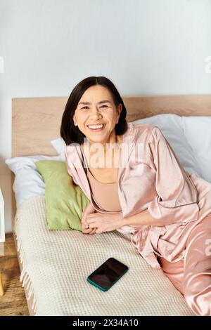 Une femme mature dans des vêtements de maison confortables est assise sur un lit à côté d'un téléphone. Banque D'Images