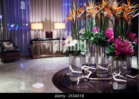 Belles fleurs dans des vases en verre sur table dans une pièce vide le soir Banque D'Images