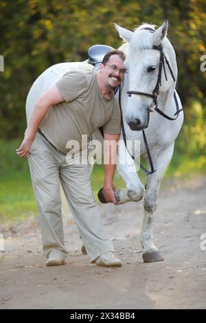 Homme heureux joue avec beau cheval blanc dans le parc d'automne ensoleillé Banque D'Images