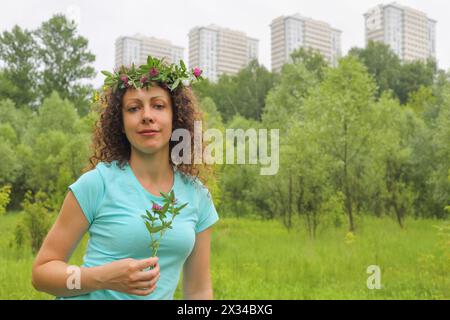 portrait demi-longueur de jeune femme avec couronne de fleurs zone boisée urbaine près du complexe d'appartements, tenant le trèfle Banque D'Images