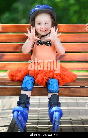 Jolie fille dans le casque et patins à roulettes se trouve sur le banc le jour d'été Banque D'Images