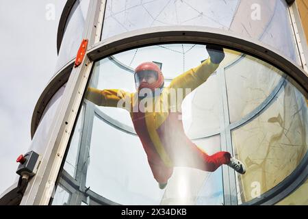 Femme en casque et costume rouge-jaune vole dans le tube d'air avec des murs de verre. Banque D'Images