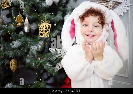 Joyeuse petite fille pose en costume de lapin près de l'arbre de noël Banque D'Images