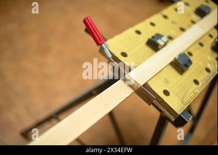 Image en gros plan d'une scie coupant un morceau de bois serré sur un établi, mettant en évidence la précision et les compétences techniques en menuiserie. Banque D'Images