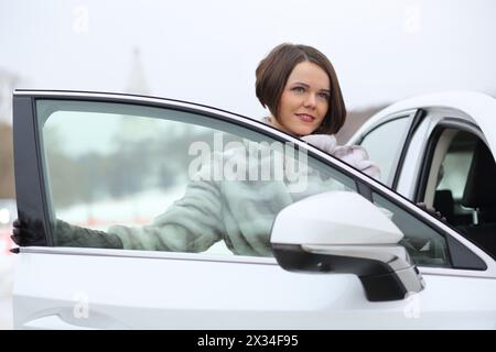 Portrait de belle fille heureuse dans une fourrure quittant la voiture blanche Banque D'Images