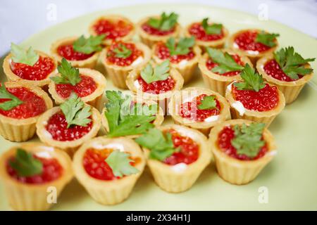 Assiette pleine de tartelettes garnies de beurre et de caviar rouge décorée de verts. Banque D'Images