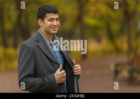 portrait demi-longueur de jeune homme en manteau gris, souriant et posant, vue de côté Banque D'Images