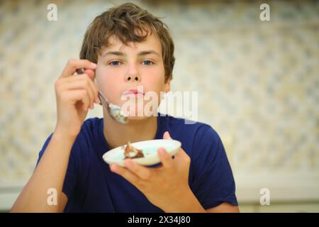 Heureux garçon adolescent mange la confection de soucoupe dans la cuisine, dof peu profond Banque D'Images