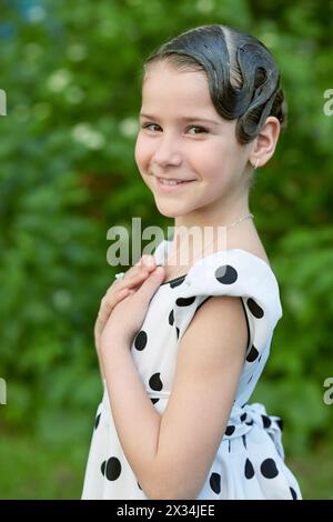 Portrait en demi-longueur d'une petite fille souriante vêtue d'une robe à pois avec coiffure. Banque D'Images