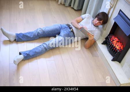 Jeune homme avec une tablette informatique couchée sur le sol près de la cheminée, vue de dessus Banque D'Images