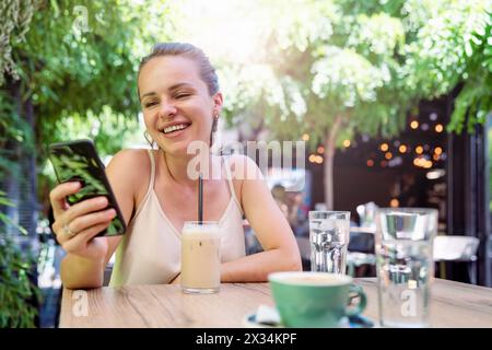 Brunette femme se détend dans un café en été et discute sur Internet à l'aide d'un smartphone. Banque D'Images