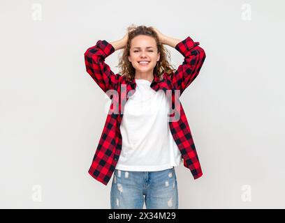 Femme heureuse tient les mains derrière sa tête souriant exprimant des émotions d'anticipation de délice devant un fond clair en studio. Banque D'Images