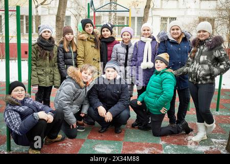 Quatre garçons sont assis squattés et huit filles se tiennent en rangée derrière eux au sportsground le jour d'hiver. Banque D'Images