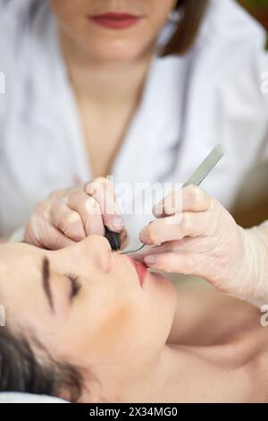 Mains rapprochées de l'esthéticienne faisant l'épilation sur la lèvre supérieure de la femme couchée sur le canapé dans le salon de beauté. Banque D'Images