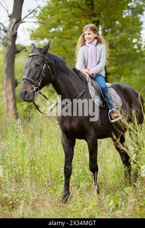 Adolescente est assise sur le cheval de châtaignier dans le parc. Banque D'Images