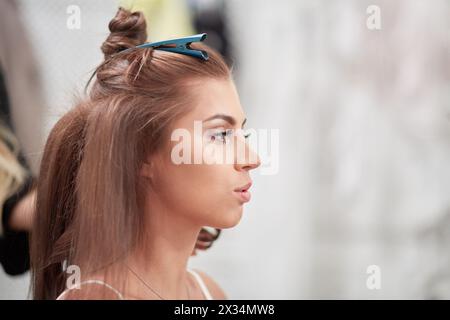 Tête dans le profil de la jeune femme tandis que visagiste fait coiffer. Banque D'Images