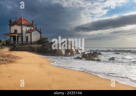 La Capela do Senhor da Pedra, une chapelle historique du XVIIe siècle, qui se dresse directement sur les rochers de la plage de Miramar au Portugal. Banque D'Images