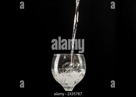 Eau tombant dans une tasse en verre. Isolé sur fond noir. Banque D'Images