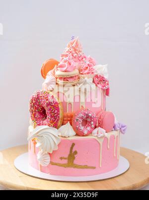 Grand gâteau rose superposé avec glaçage rose, cake POPS, macarons, meringues, beignets et figure dorée de fille gymnaste Banque D'Images