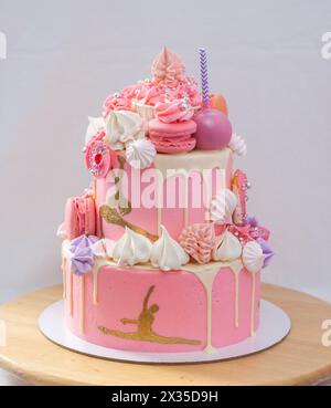 Grand gâteau rose superposé avec glaçage rose, cake POPS, macarons, meringues, beignets et figure dorée de fille gymnaste Banque D'Images