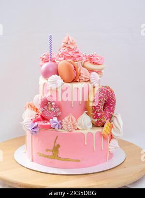 Grand gâteau rose superposé avec glaçage rose, cake POPS, macarons, meringues, beignets et figure dorée de fille gymnaste Banque D'Images