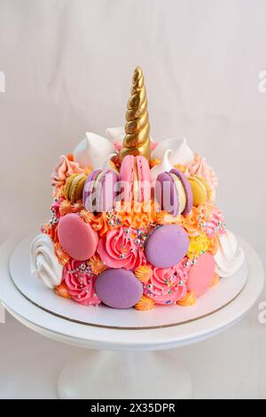 Gâteau de licorne avec corne fondante dorée, cils et glaçage au fromage à la crème rose, orange, violet sur fond neutre Banque D'Images