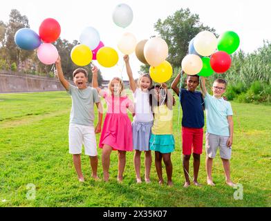 Joyeux préadolescents garçons et filles avec des ballons colorés sur la pelouse verte Banque D'Images