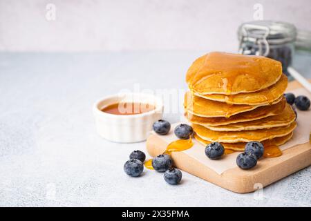 Planche en bois de crêpes savoureuses avec des myrtilles et du sirop d'érable sur fond blanc Banque D'Images