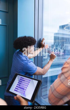 Jeune homme biracial écrivant sur des graphiques sur la fenêtre dans un bureau moderne Banque D'Images