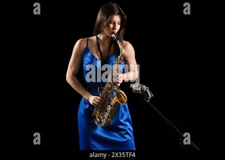 Belle femme avec microphone jouant du saxophone sur fond sombre Banque D'Images