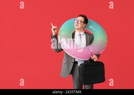 Travailleur de bureau avec index relevé et anneau gonflable rêvant de vacances sur fond rouge Banque D'Images