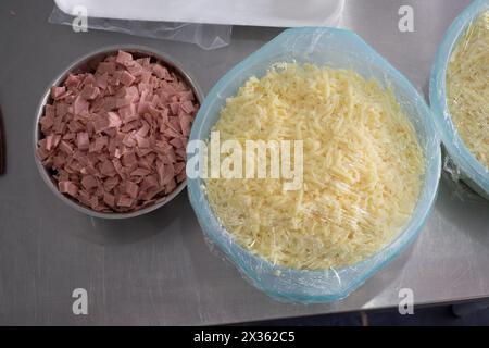 Un bol de jambon et de fromage est assis sur une table à côté d'un autre bol de fromage. Le jambon est coupé en petits morceaux et le fromage est en pile. La table est ma Banque D'Images