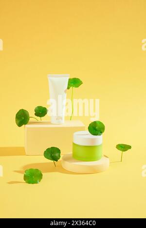 Vue de face de l'ensemble de bouteille cosmétique et pot placé sur des podiums beiges et des feuilles fraîches de centella asiatica sur fond jaune. Scène minimale pour la publicité Banque D'Images
