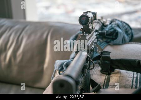 un fusil d'assaut avec vue optique sur le canapé à côté de la fenêtre, faible profondeur de champ Banque D'Images