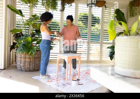 Mère biraciale mature, fille adulte peignent des meubles dans un projet d'upcycling à la maison Banque D'Images