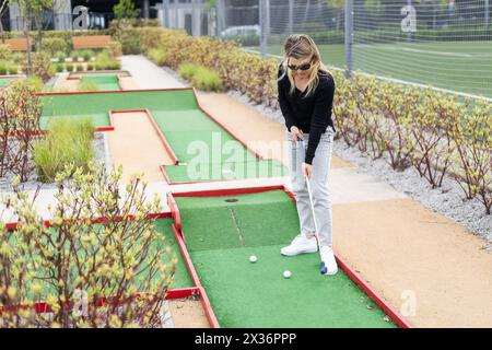 Femme jouant au mini golf et essayant de mettre la balle dans le trou. Activités de loisirs estivales Banque D'Images