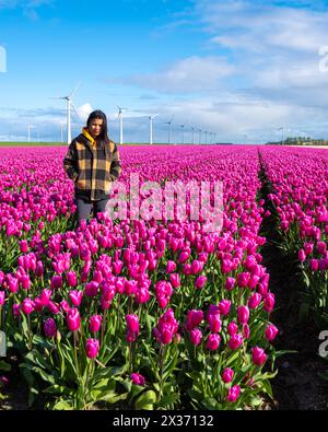 Une femme asiatique se tient gracieusement debout dans un vaste champ de tulipes violettes vibrantes, embrassant la beauté de la nature en pleine floraison. Banque D'Images