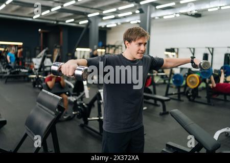 Portrait d'un sportif débutant motivé ayant du mal à faire un exercice d'élévation de bras latéral avec des haltères. Athlète masculin fatigué améliore les épaules avec Banque D'Images