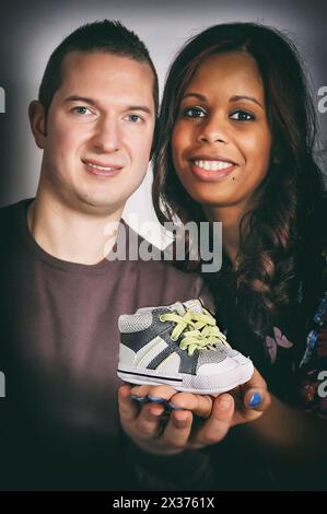 Heureux couple multiracial tenant une chaussure de bébé dans leurs mains Banque D'Images