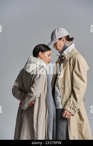 Un jeune couple élégant en trench-coat debout ensemble dans un studio sur un fond gris. Banque D'Images