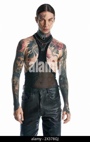 Un jeune homme avec une abondance de tatouages ornant son corps pose avec confiance dans un cadre de studio sur un fond gris. Banque D'Images