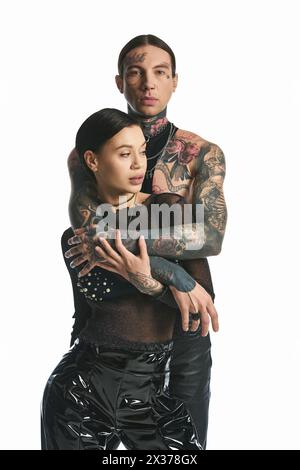 Un jeune couple élégant avec des tatouages complexes sur les bras pose dans un studio sur un fond gris. Banque D'Images
