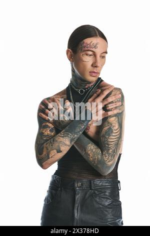 Un jeune homme avec des tatouages ornant ses bras et sa poitrine pose élégamment dans un studio sur un fond gris. Banque D'Images