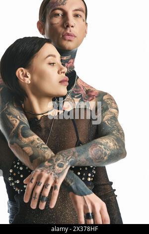 Un jeune couple élégant avec des tatouages sur les bras pose dans un studio sur un fond gris. Banque D'Images